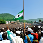 **

"A historical scene depicting Sierra Leone's independence day celebrations on April 27, 1961.  A crowd of jubilant, fully clothed Sierra Leoneans in modest traditional attire are waving flags in Freetown. Sir Milton Margai is giving a speech. In the background, the British flag is being lowered and the Sierra Leone flag is being raised.  Clear blue sky, bright daylight.  Safe for work, appropriate content, professional, family-friendly, perfect anatomy, correct proportions, natural pose, well-formed hands, proper finger count, natural body proportions."

**